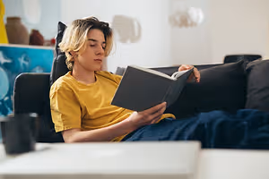 A young boy sits on a couch and reads a book