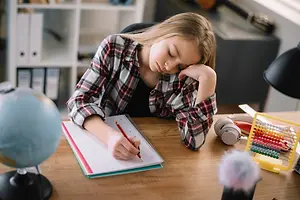 A girl sleeping on her desk while holding a pen in her hand