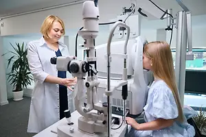 A woman doctor is examining the eyes of a young girl using an eye exam machine in a clinic.