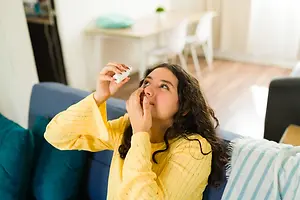 A girl is sitting on the couch, holding a tube, and seems to be blowing her nose while looking upward