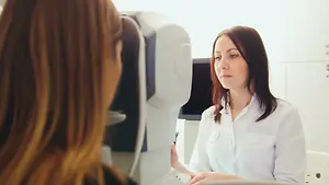 A woman in a white lab coat examines a patient's eye using a medical device.
