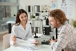 An optometrist is performing an eye examination for a male patient in an office setting.