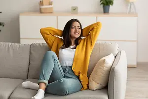 A woman sitting on a couch with her arms behind her head and a smile on her face