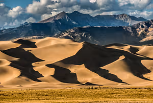 A large desert with sand dunes and mountains in the background under a cloudy sky