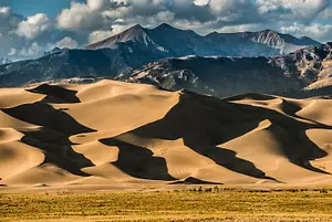 A large desert with sand dunes and mountains in the background under a cloudy sky