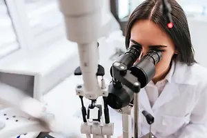 A woman is looking through an ophthalmoscope, possibly in a laboratory.