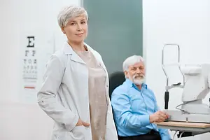 A man in a blue shirt is sitting in front of an eye chart while a woman in a white coat is standing next to him.
