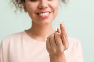 A woman holding a contact lens in her hand