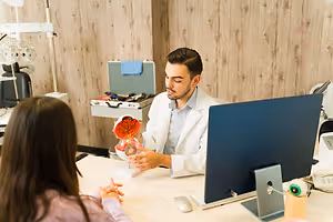 A doctor in a white coat explains an eye model to a woman in a medical office.