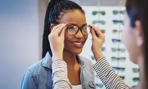 A woman is trying on glasses with the help of another woman in a store with many glasses on display