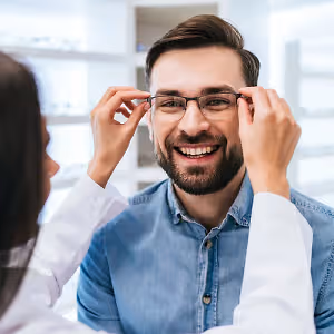 Man smiling while adjusting glasses in a professional setting
