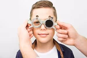 A young boy wearing glasses with a cross symbol on the side, being examined by a person.