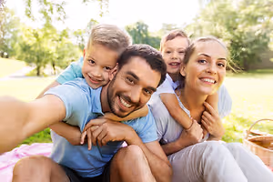A family of four, two kids and two adults, sitting on a grassy field with a picnic basket and smiling for a photo