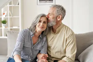 A man and woman are sitting on a couch, the man is kissing the woman's forehead