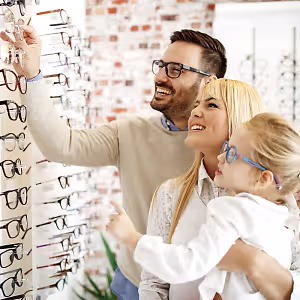 A family of three standing in front of a display of glasses and smiling at the camera