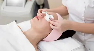 Woman at a spa getting an eye treatment from a woman in a white uniform