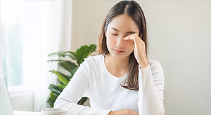 Asian woman with a headache sitting at a desk