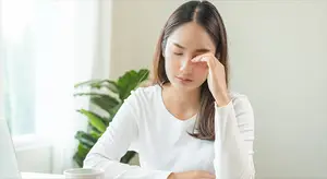 Asian woman with a headache sitting at a desk