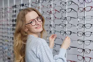 A woman wearing glasses is looking at glasses on a rack in a shop