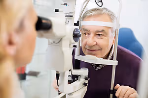 An elderly man is having his eyes examined by an optometrist in a clinic.