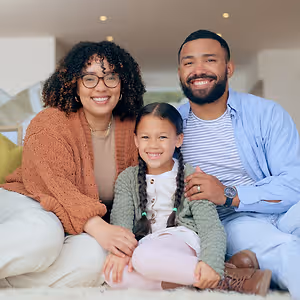 A family sitting on the floor with a girl smiling in between a man and a woman