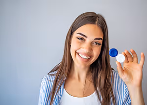 A woman with brown hair is smiling and holding a blue and white bottle in her hand. She is posing for a picture.