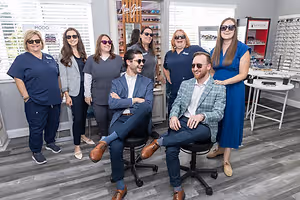 A group of people are smiling and posing for a photo in an optical shop.