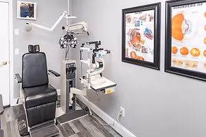 An eye exam chair and an ophthalmoscope on the side of a gray wall with posters and a picture frame