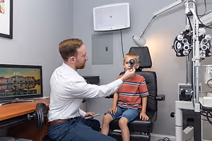 A man is sitting on a chair and holding an ophthalmoscope to a boy's face