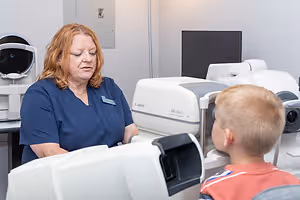 A woman in a blue uniform is conducting an eye examination on a young boy using a Canon eye exam machine.