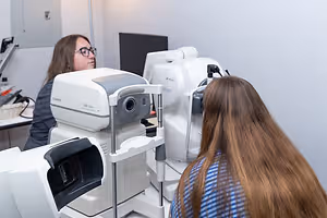 Two women are checking their eyes with a Canon machine in a medical room