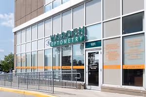 An office building with the name Warden Optometry on the glass windows and a glass door with a sign that reads Welcome New Patients.