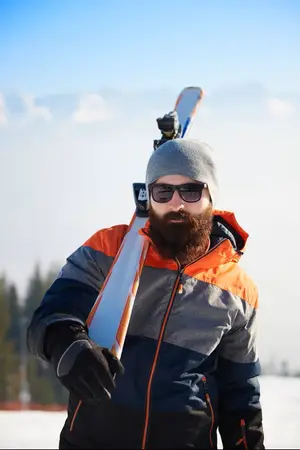 Man holding two skis in his hands on a snowy slope