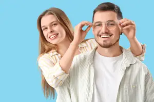 A man with glasses on and a woman adjusting them on his head.