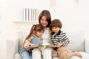 A woman is reading a book to two children on a couch.