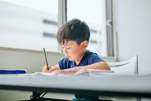 A boy is doing his homework at a desk in a classroom