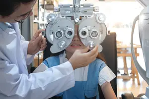 A child is sitting in a chair and having her eyes examined by a doctor wearing a white coat.
