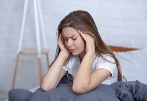 Young woman sitting in bed looking tired and holding her head