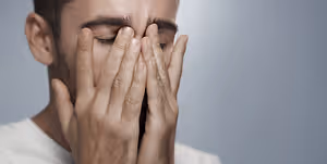 A man is covering his face with his hands, looking like he is in pain or discomfort.