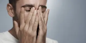 A man is covering his face with his hands, looking like he is in pain or discomfort.
