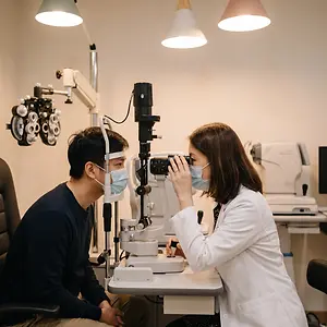 A patient is having an eye test with a doctor wearing a face mask and a lab coat
