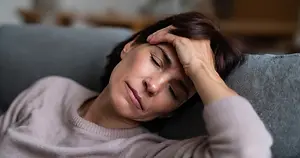 woman laying down on a couch holding her head with her hand looking in pain
