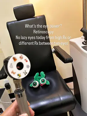 An eye exam is being conducted in a room with a black chair and a green toy on it. The text above the chair reads, 'What's the eye power? Retinoscopy No lazy eyes today from high Rx or different Rx between two eyes.'