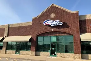 A brick building with a sign that says Visionary Eyecare on the front, two awnings, and a glass door with a green door handle and a window with blinds