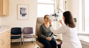 An older woman is having her eyes checked by a woman in a white coat at an eye doctor's office.