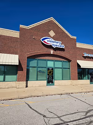 A brick building with a glass door and windows, a sign above the door reads 'Visionary Eyecare', and a wreath is placed in front of the door.