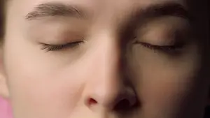 A close up of a girl with her eyes closed and slightly open mouth. She has long eyelashes and a slight frown on her face. She is probably sleeping or resting. Her face is slightly blurred, and the light is shining on her face. She is wearing a pink shirt. The background is dark. The image is slightly blurry.