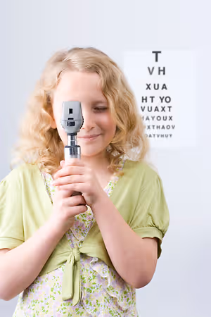 A little girl is holding a black and silver eyeglass that is used for eye examination in a room