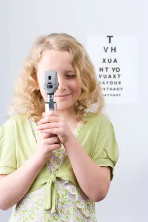 A little girl is holding a black and silver eyeglass that is used for eye examination in a room