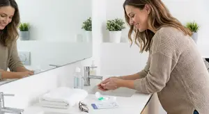 A woman smiling and washing her hands in front of a mirror